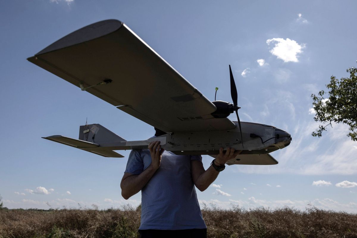 Person holding a large drone outdoors under a sunny, partly cloudy sky.