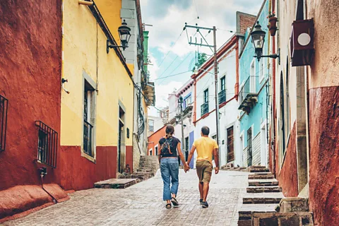 Getty Images Two people walk hand in hand along a cobbled street lined with colourful buildings