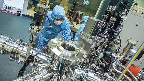 Researcher in lab suit examining large cylindrical metal machine