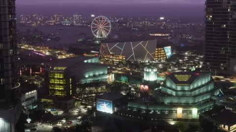 Aerial night view of downtown Vice City with illuminated Ferris wheel and stadium